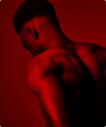 A photo of a man's shoulders, upper back and head, bathed in a red wash of light on a red background.