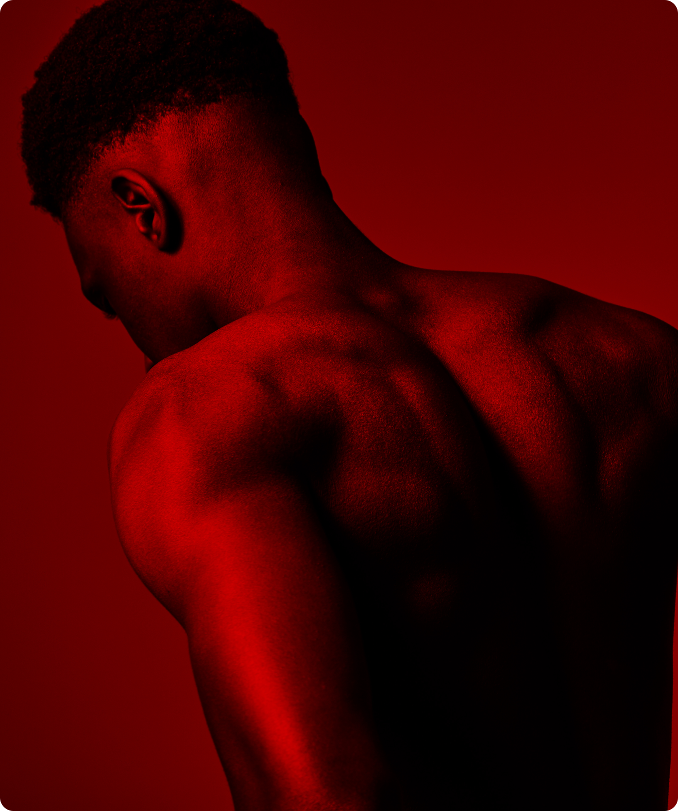 A photo of a man's shoulders, upper back and head, bathed in a red wash of light on a red background.