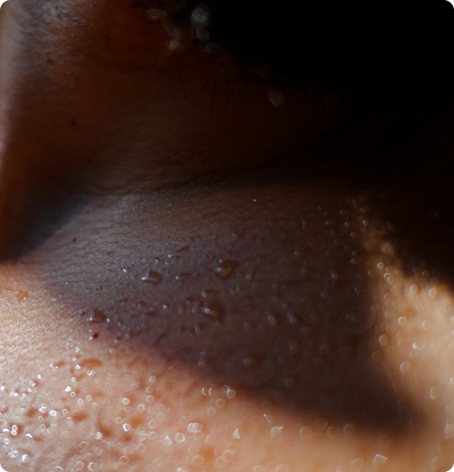 A close up macro shot of the back a person's neck & upper shoulders with sweat beading on their skin.