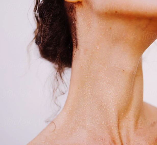 A close up photo of a woman's chin, neck and collar bones with sweat beading on her skin.
